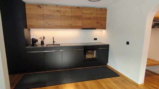 A modern kitchen with dark cabinetry, a built-in oven, and a wooden countertop. - Casa Suvita / Alpine Luxury Apartment (Obersaxen Mundaun)