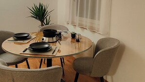 A dining area with a round glass table, four grey chairs, a potted plant, and a window with sheer curtains. - Casa Suvita / Alpine Luxury Apartment (Obersaxen Mundaun)