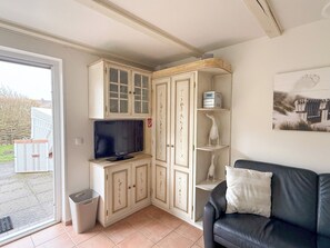 Ein Wohnzimmer mit einer schwarzen Ledersofa, einem Fernseher auf einer Kommode und einer weißen Kommode mit Glastüren.