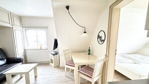 Una stanza compatta con un letto, una scrivania con sedia, un tavolino, un termosifone e una finestra.