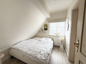 A bedroom with a bed, a radiator, a window with curtains, and a door. - House Inselfriede Pidder Lüng 5: 300 m to the beach in Westerland (Westerland)