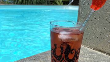 A glass with an octopus design and a red fruit garnish by a pool with clear blue water and a tropical background.