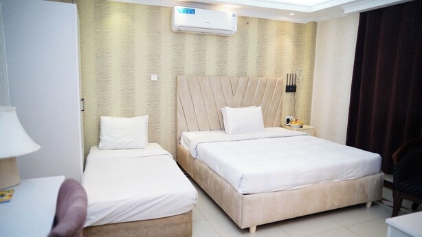 A hotel room with two beds, a desk, a chair, an air conditioning unit, and a patterned wall. - 1-bedroom hotel in enchanting Dhaka with fitness room and AC (Dhaka)