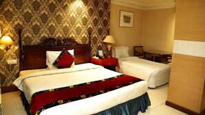 A hotel room with two beds, a wooden headboard, a red and blue bedspread, a nightstand with a lamp, a framed picture on the wall, and a wooden table. - 1-bedroom hotel in enchanting Dhaka with fitness room and AC (Dhaka)