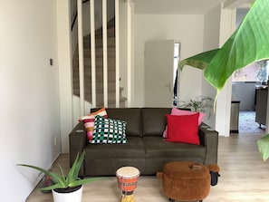 Una sala de estar con un sofá, un tambor, una planta en maceta y una hoja verde grande.