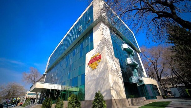 A modern building with a glass facade, a prominent logo on the side, and a clear sky. - ASTRA HOTEL (Almaty)