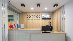 A reception desk with a computer, a clock, and flags of various countries. - ASTRA HOTEL (Almaty)