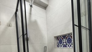 Une douche équipée d’un pommeau de douche à main, d’un panneau de commande fixé au mur et d’une petite mosaïque décorative.