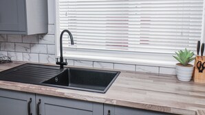 Een keuken met een zwarte spoelbak, een houten aanrechtblad en een marmeren spatwand, en een raam met jaloezieën.