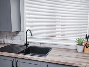A kitchen with a black sink, wooden countertop, marble backsplash, and a window with blinds. - 34 Fountain Close (Whitby)