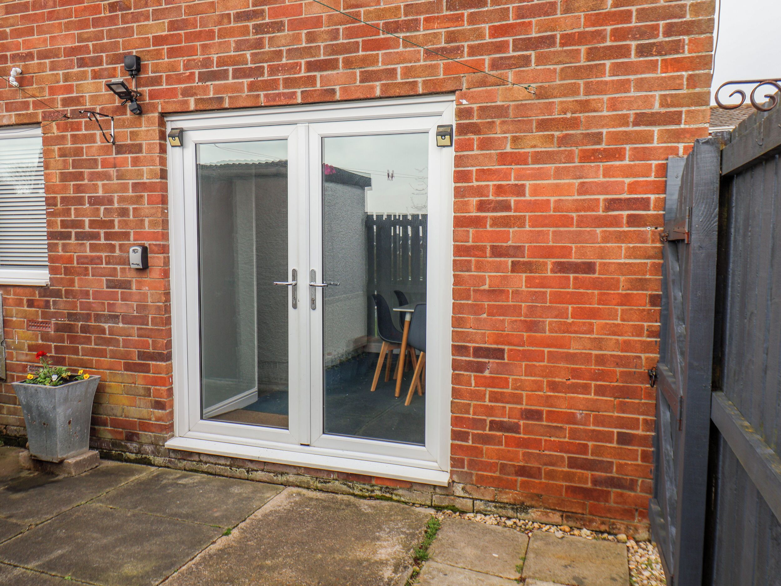 A brick house with a white-framed glass door, a small garden, and a wooden chair outside.