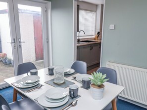 Uma sala de jantar com uma mesa posta para quatro pessoas, um vaso de planta e vista para a cozinha.