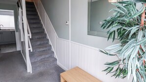 Een trap met witte leuningen die uitkomt op een plateau, met een houten bankje, een spiegel aan de muur en een potplant.