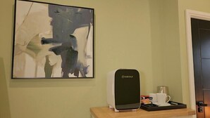 Eine Kaffeemaschine auf einem Tablett mit einer Tasse und einem kleinen Gegenstand, ein gerahmtes abstraktes Gemälde an der Wand und eine Tür mit Griff.