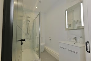 A modern bathroom with a glass shower enclosure, a white sink with a mirror above, and a toilet. - The Tall Trees Hotel (Amlwch)