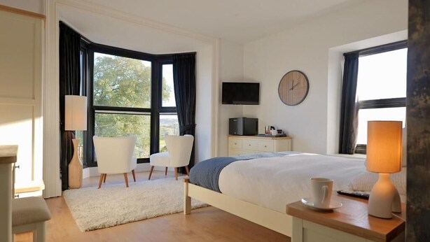 Ein Schlafzimmer mit Bett, Stuhl, Fernseher, einer Uhr und einem Fenster.