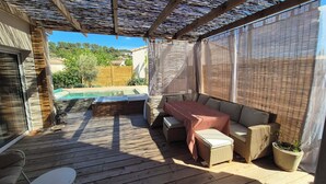Een overdekt terras buiten met een zwembad, een zithoek en een bloempot.
