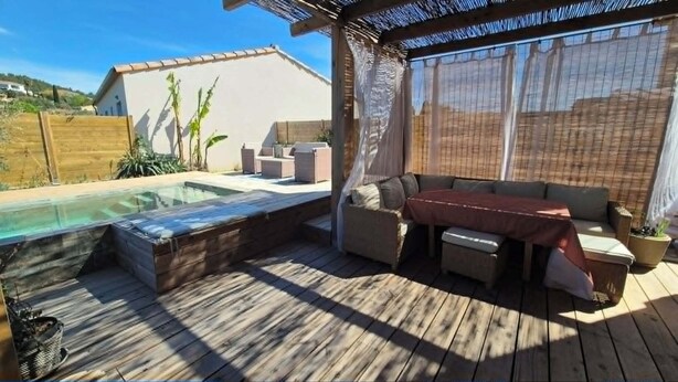 Een houten terras met een jacuzzi, buitenmeubels en uitzicht op een heuvel.