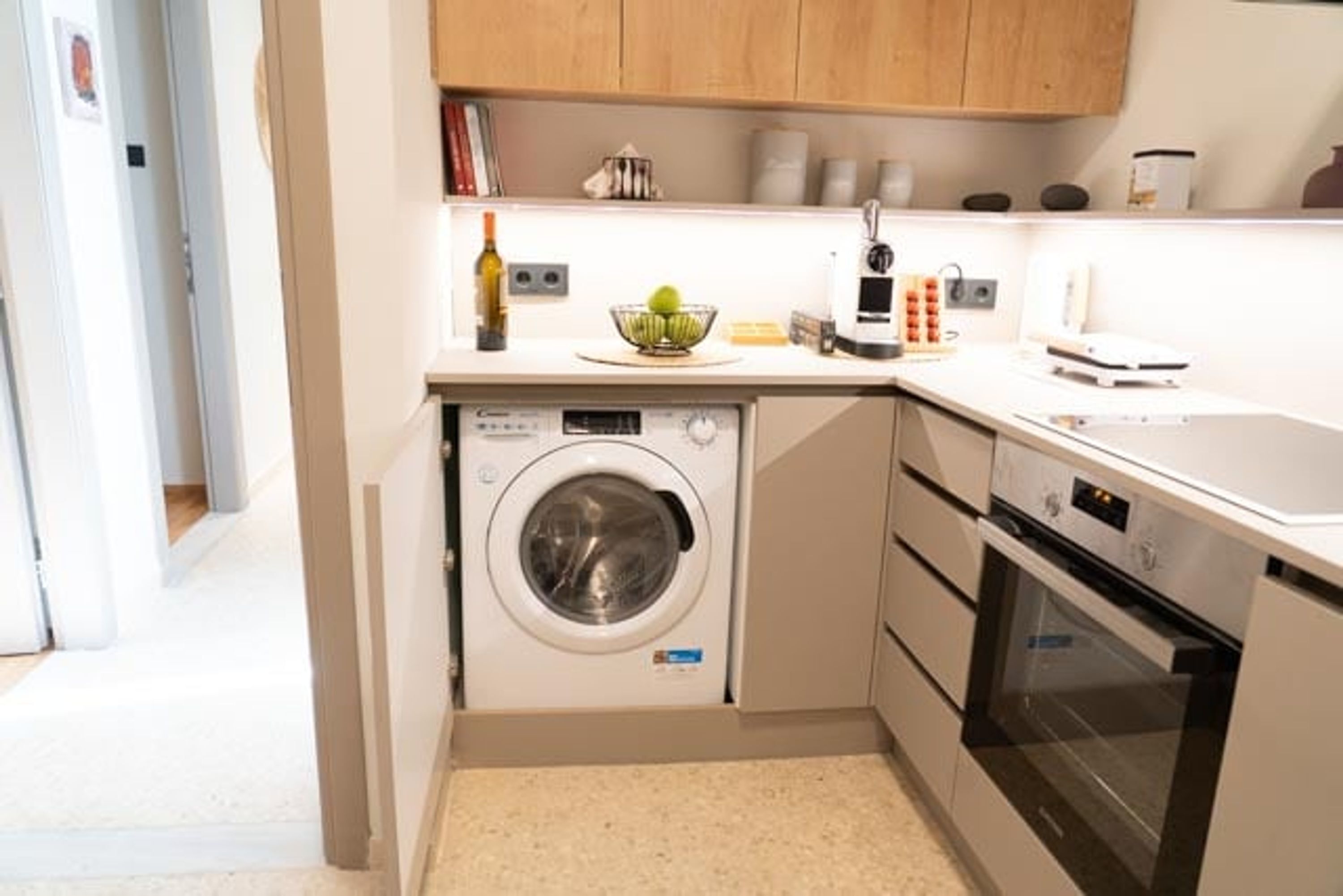 A compact kitchen with a washing machine, oven, and a countertop with various appliances and items.