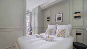 A neatly made bed with towels and a bottle, a black chair, and a framed picture on the wall. - Charming apartment 2BDR/6PAX in the heart of Paris (Paris)