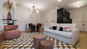 Uma sala de estar com um sofá branco, uma poltrona rosa, uma mesa de jantar com cadeiras e um tapete estampado.