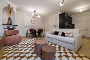 Ein Wohnzimmer mit einem weißen Sofa, einem rosa Sessel, einem Esstisch mit Stühlen und einem gemusterten Teppich.