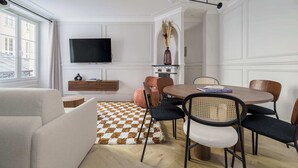 Uma sala de estar moderna com sofá, mesa de jantar com cadeiras, televisão na parede e tapete estampado.