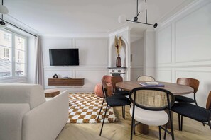 Ein modernes Wohnzimmer mit einer Couch, einem Esstisch mit Stühlen, einem an der Wand montierten Fernseher und einem Teppich mit Muster.