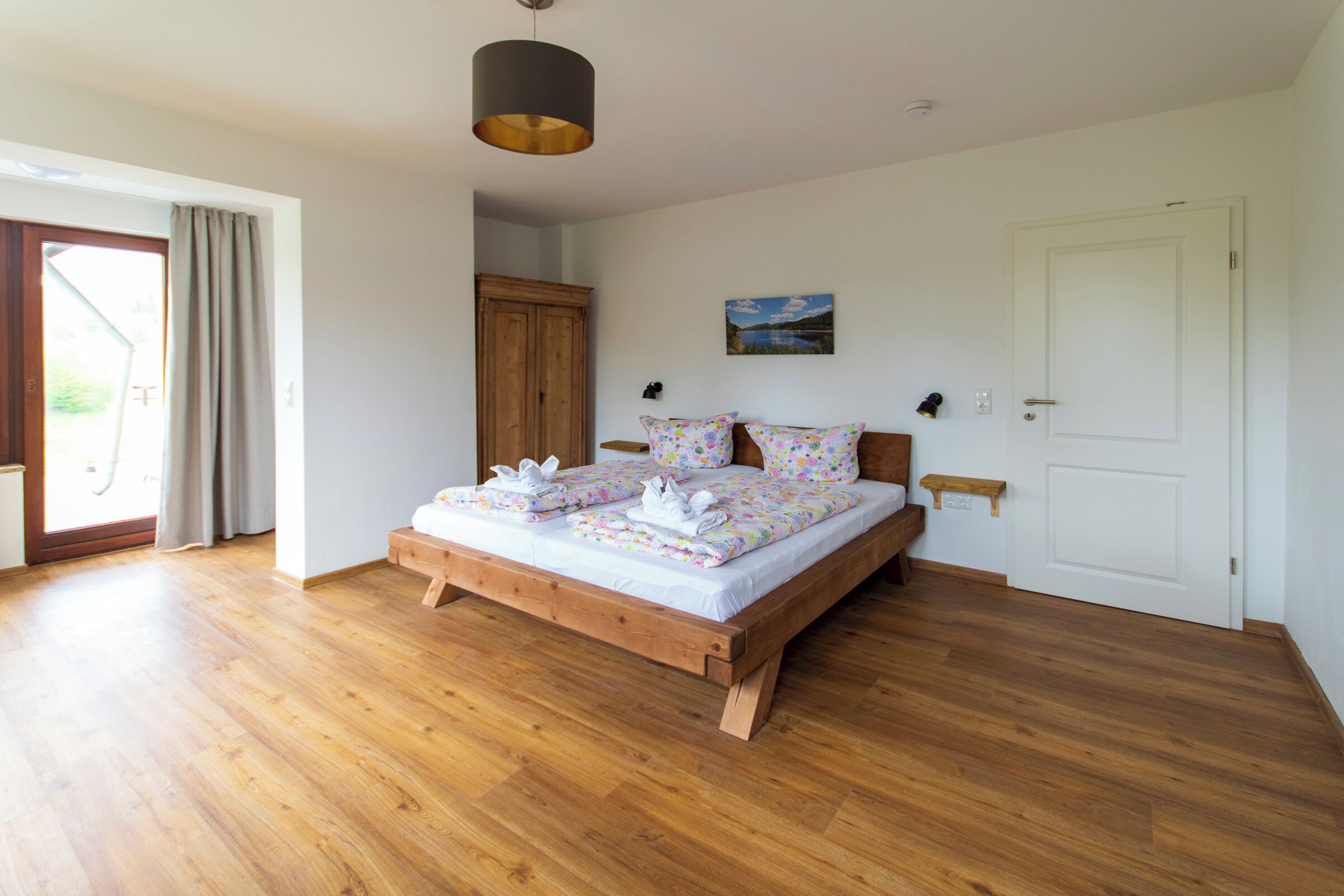 A bedroom with a wooden bed, a large window, and a door.