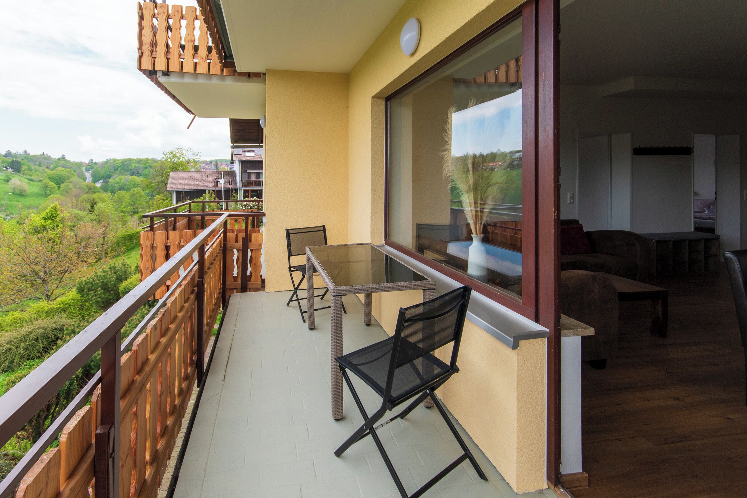 A balcony with a table and chairs, overlooking a green landscape.