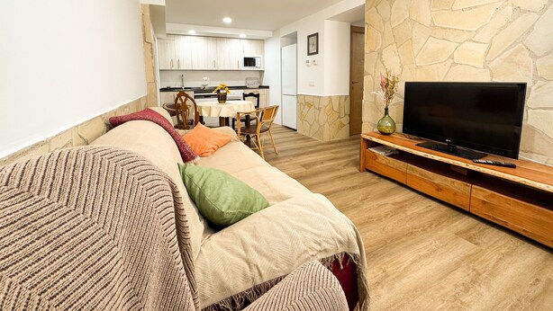 A living room with a sofa, a television, and a stone wall.