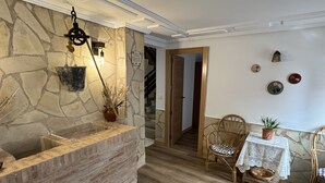 A stone reception desk with a hanging light fixture, a wicker chair, a small table with a plant, and a staircase in the background.