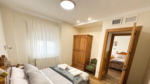 A bedroom with a bed, a wooden wardrobe, a chair, and a small table with a plant.