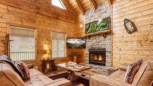 L’intérieur d’une cabane en rondins, avec une cheminée en pierre, des canapés en cuir, une table basse et une grande fenêtre.