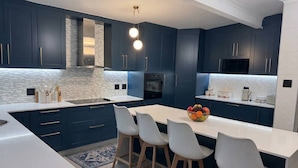 Een moderne keuken met donkerblauwe kastjes, witte aanrechtbladen en een centraal eiland met barstoelen.
