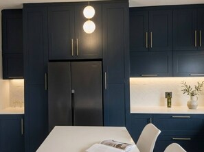 A modern kitchen with dark cabinetry, a stainless steel refrigerator, and pendant lighting.
