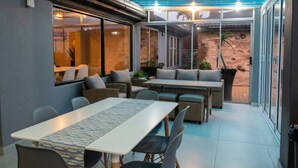 Een overdekte patio met een tafel en stoelen, een bank en uitzicht op het buiten.