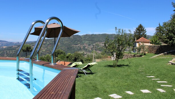 A swimming pool with a wooden deck, a metal ladder, and a view of a hillside.