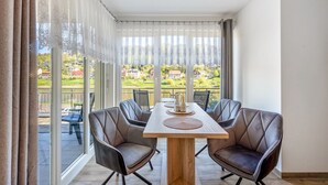 Ein Essbereich mit Tisch und Stühlen, großen Fenstern mit Vorhängen und Blick auf Grünflächen sowie Gebäude.