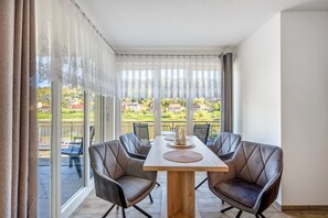 A dining area with a table and chairs, large windows with curtains, and a view of greenery and buildings outside. - Apartment 'Ferienwohnung Elbufer 3a' with Mountain View, Private Terrace and Wi-Fi (Stadt Wehlen)