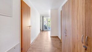 Ein Flur mit Holzboden, weißen Wänden und Blick auf einen Außenbereich mit Tischen und Stühlen.