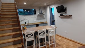 A kitchen with a wooden table and white chairs, a built-in stove, and a TV mounted on the wall. - Casas do Pargo- Palheiro (Lombada Velha)