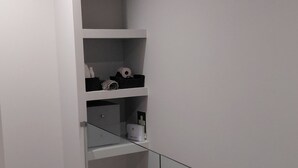 A room with a wooden floor, white walls, and a glass partition. There are shelves with various items on them. - Casas do Pargo- Palheiro (Lombada Velha)