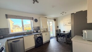A modern kitchen with a dishwasher, washing machine, and a dining area with a table and chairs. - Inverness Retreat, visit the capital of the Highlands and relax! (Inverness)