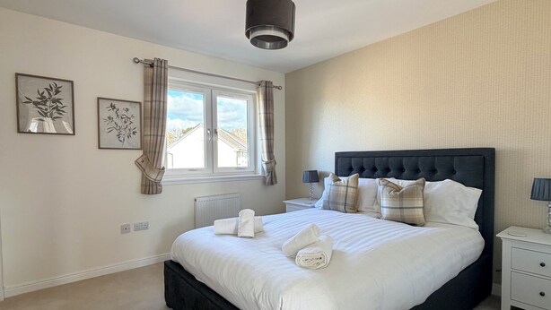 A bedroom with a large bed, a bedside table, a nightstand, a window with curtains, and two wall-mounted artworks. - Inverness Retreat, visit the capital of the Highlands and relax! (Inverness)