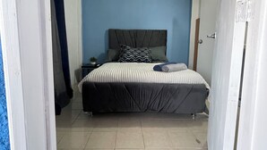 Un dormitorio con cama, mesita de noche, planta en maceta y felpudo.