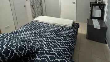 A bedroom with a bed, a bedside table, a TV, and an air conditioning unit.