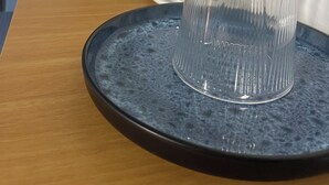 Una kitchenette con una cafetera, un vaso sobre una bandeja y una taza en un platillo.