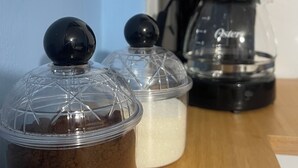 Una encimera de cocina con una cafetera, un recipiente con líquido marrón y un recipiente con líquido blanco.