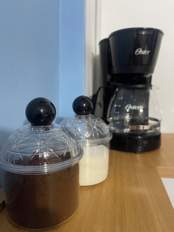 Una encimera de cocina con una cafetera, un recipiente con líquido marrón y un recipiente con líquido blanco.
